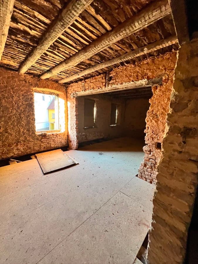 Entkerntes Dachgeschoss mit freigelegter Holzbalkendecke und Bruchsteinwand