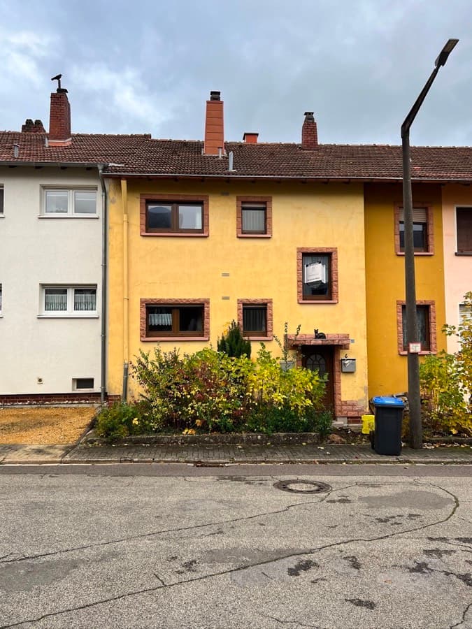 Gelbes Reihenmittelhaus mit altem Fensterbestand von der Straße aus
