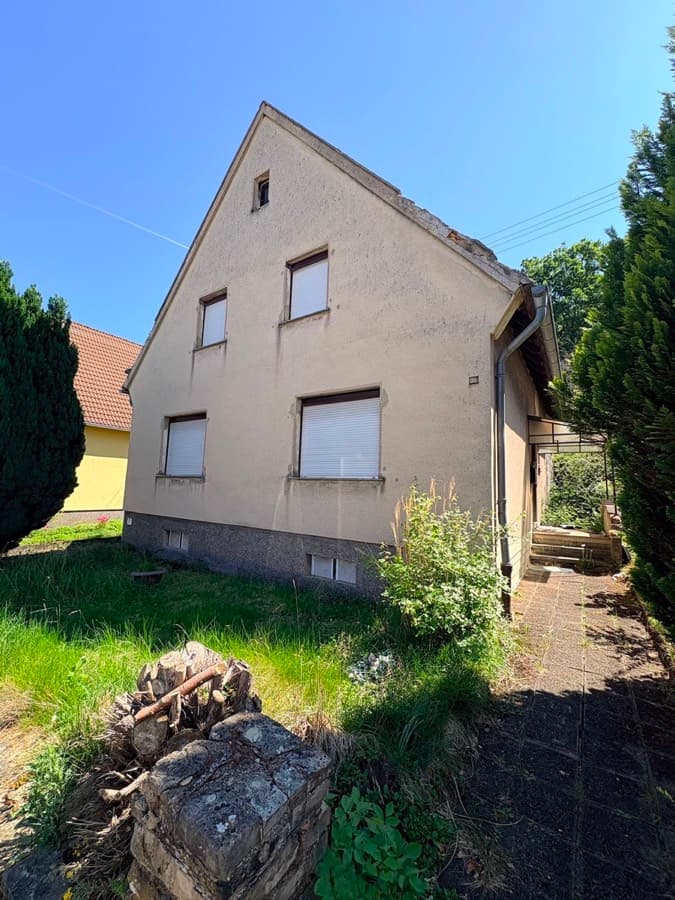 Freistehendes Einfamilienhaus mit Satteldach und verwildertem Garten vor der Sanierung